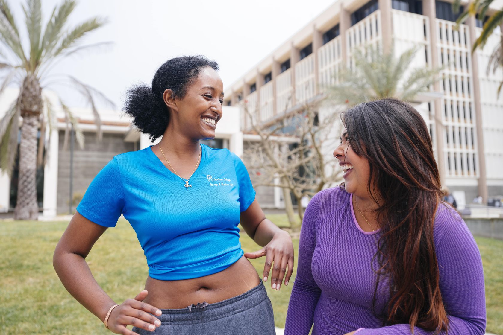 Two students laugh together while standing outside the UCSB Library near the Arbor.